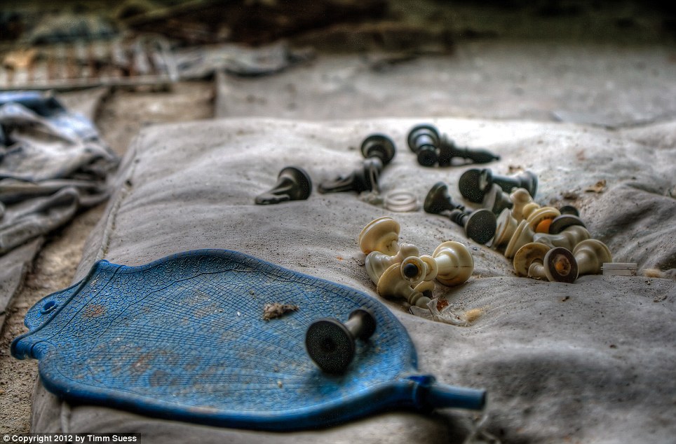 A flattened dust-covered water bottle lies strewn on a mattress left on the ground alongside several black and white pieces of a chess set. At least 28 people have died of acute radiation sickness from close exposure to the shattered reactor